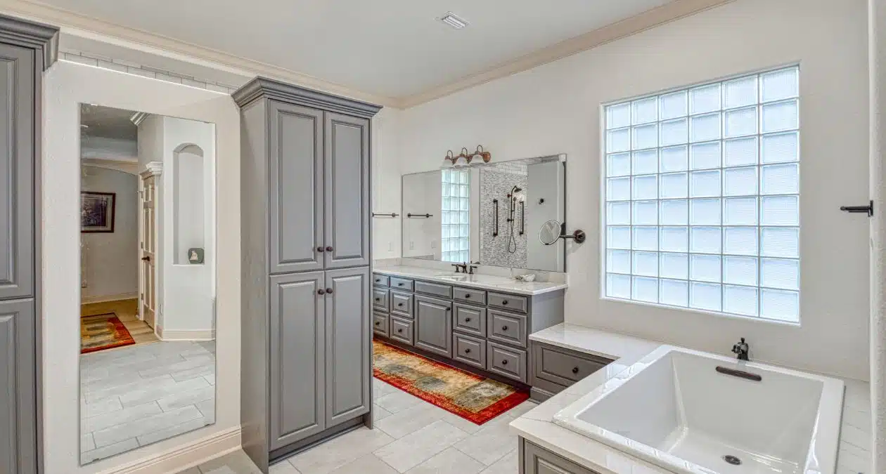 herringbone tile shower with brass fixtures beside white quartz vanity with gold faucet in Craft Bathroom