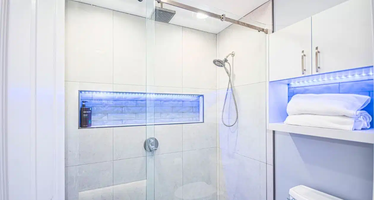 herringbone tile shower with brass fixtures beside white quartz vanity with gold faucet in Craft Bathroom